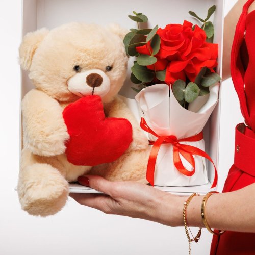 Roztomilý plyšový medvedík, ktorý sa spolu s krásnymi ružami ukrýva v krásnom bielom boxe s výrezom v tvare srdca. Ideálna voľba na Valentín.