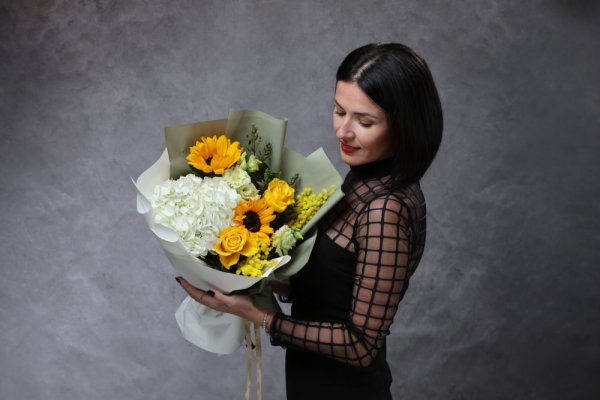 Kontrastná kytica so žltými slnečnicami, veľkou bielou hortenziou, žltými ružami a mimózou v elegantnom dekoračnom papieri.
